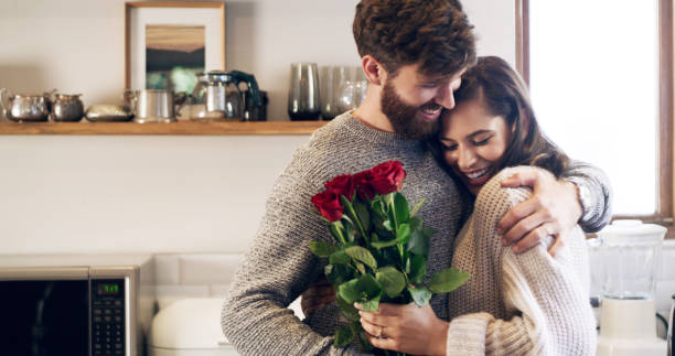 Shot of a young man surprising his wife with a bunch of roses at home